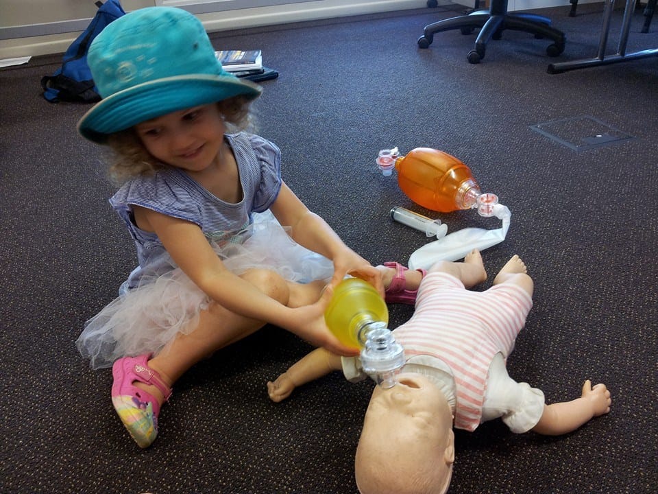 A little girl trying to ventilate a baby manikin.